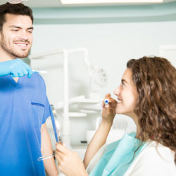 Dentist showing technique of brushing teeth to his female patient in dental clinic.